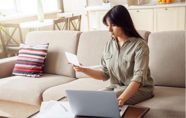 Woman holding bill in front of laptop
